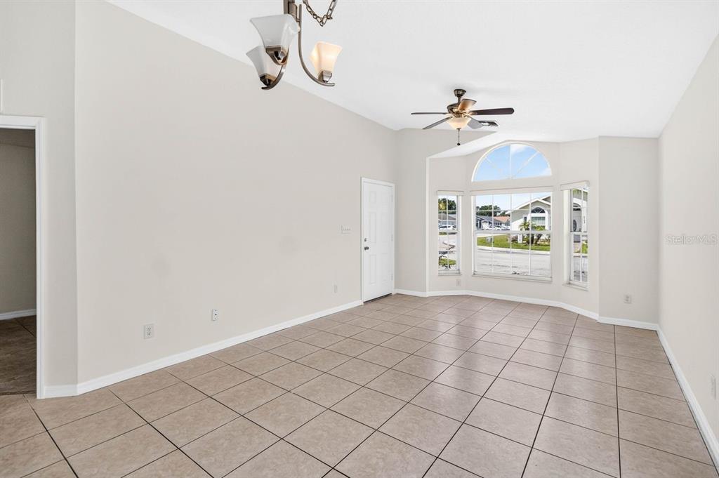A bright, empty room features light-colored tile flooring, a ceiling fan, and a bay window — 2382 HARBOR TOWN DRIVE, KISSIMMEE, FL