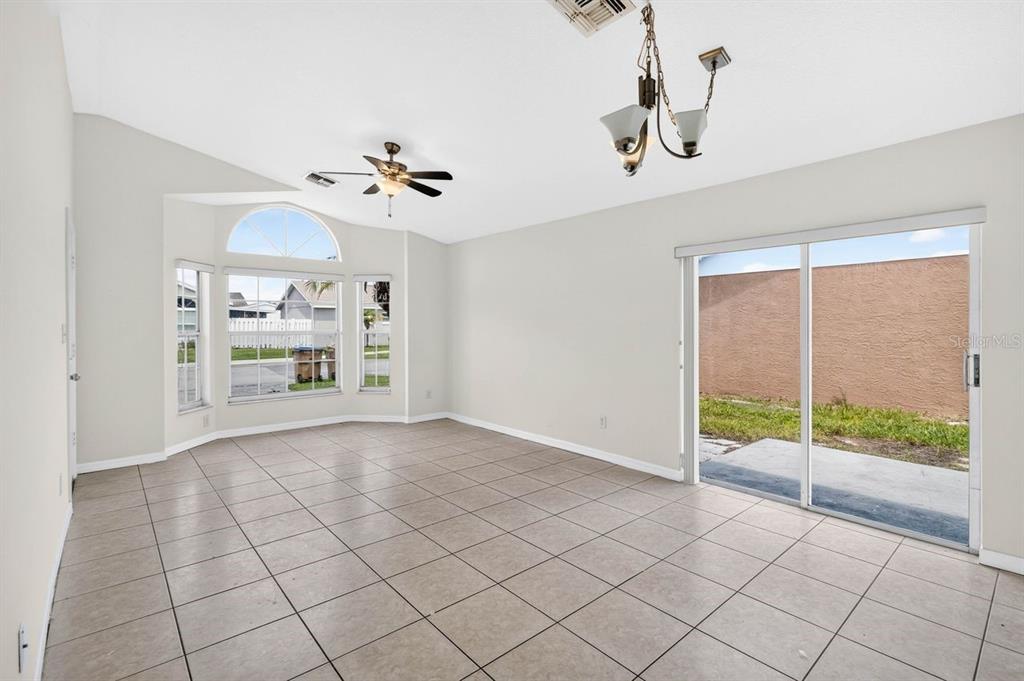 A bright living room features tile flooring, a ceiling fan, a chandelier, and sliding glass doors — 2382 HARBOR TOWN DRIVE, KISSIMMEE, FL