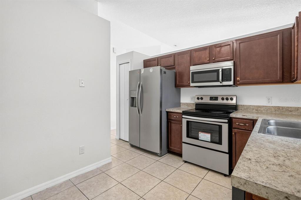 A kitchen features stainless steel appliances, dark wood cabinets, and light-colored tile flooring — 2382 HARBOR TOWN DRIVE, KISSIMMEE, FL