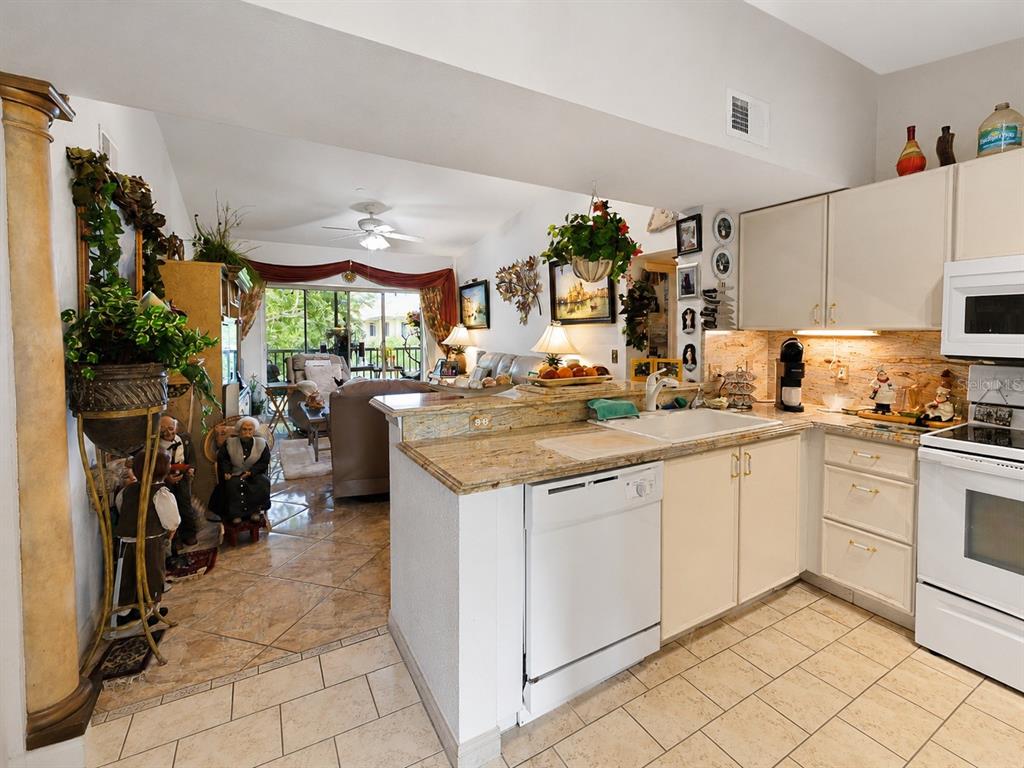 A kitchen with white cabinets and granite countertops overlooks a living area with tile floors — 8294 KEY ROYAL CIRCLE UNIT 1631, NAPLES, FL