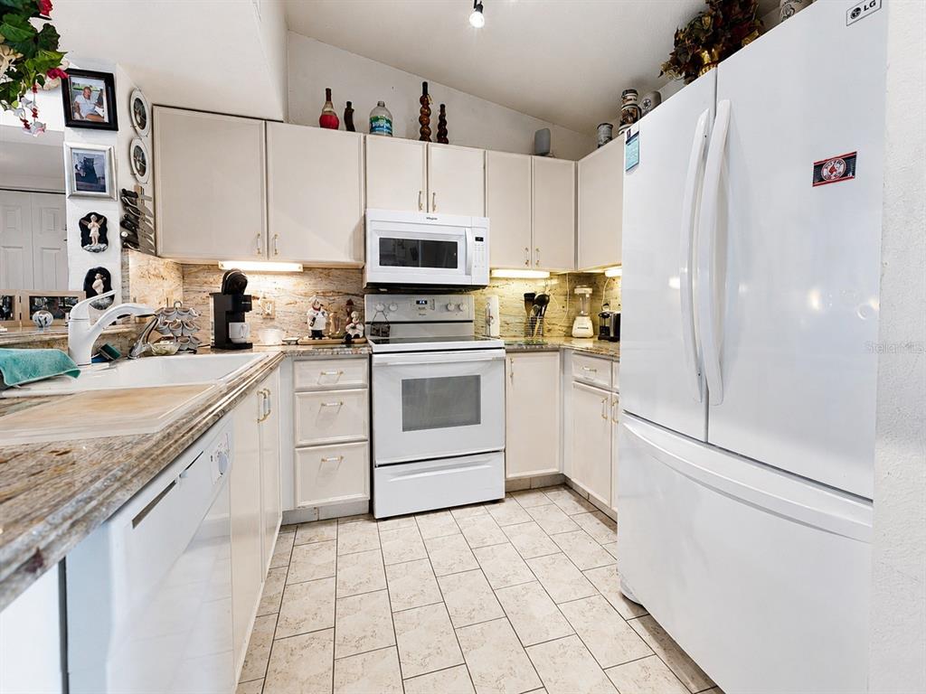 A kitchen features white cabinetry, white appliances, tiled flooring, and granite countertops — 8294 KEY ROYAL CIRCLE UNIT 1631, NAPLES, FL