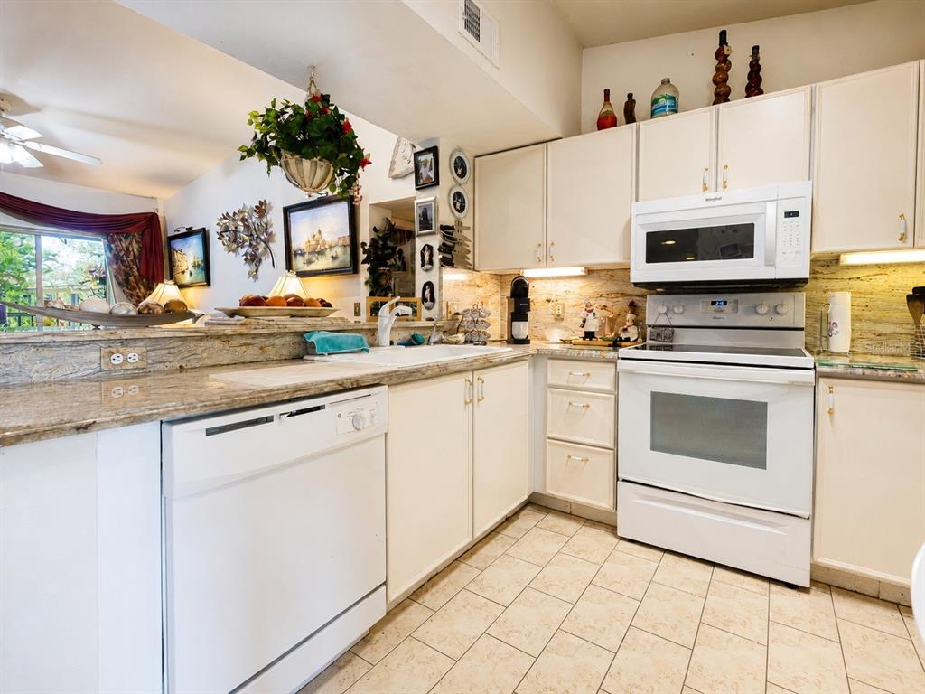 A kitchen features white cabinets, a white dishwasher, a white range, and granite countertops — 8294 KEY ROYAL CIRCLE UNIT 1631, NAPLES, FL