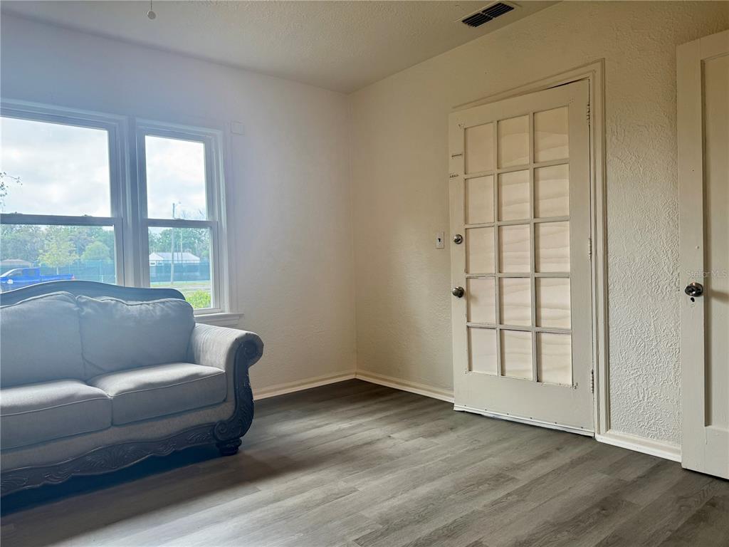 A room with gray wood-look flooring, a gray sofa, a window, and a glass-paneled door — 425 E SESSOMS AVENUE, LAKE WALES, FL