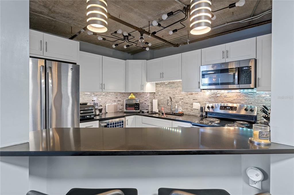 A kitchen features white cabinetry, stainless steel appliances, a dark countertop, and exposed ceiling pipes — 400 E COLONIAL DRIVE UNIT 207, ORLANDO, FL