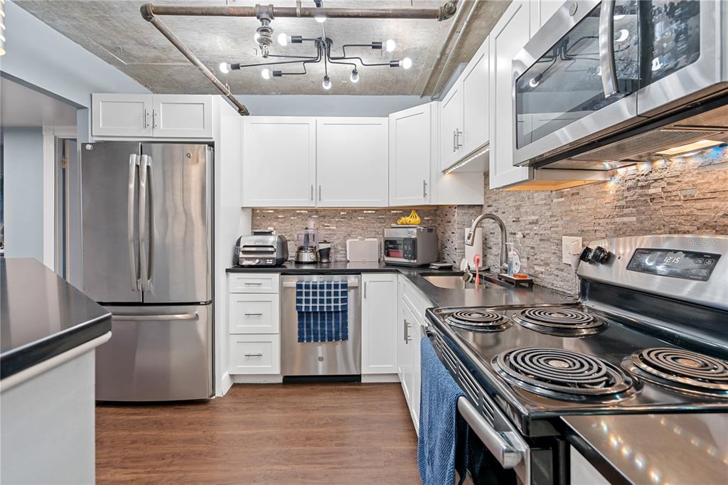 A kitchen with white cabinets, stainless steel appliances, dark countertops, and an exposed concrete ceiling — 400 E COLONIAL DRIVE UNIT 207, ORLANDO, FL