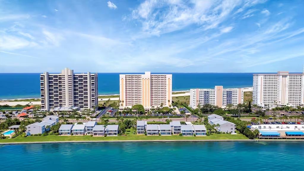 An aerial view shows several multi-story apartment buildings situated along a coastline with blue water — 1270 GULF BOULEVARD UNIT 701, CLEARWATER BEACH, FL