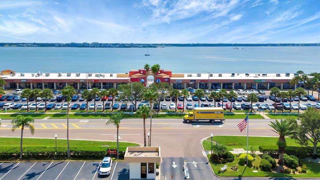 An aerial view shows a waterfront shopping center with a parking lot and a road — 1270 GULF BOULEVARD UNIT 701, CLEARWATER BEACH, FL