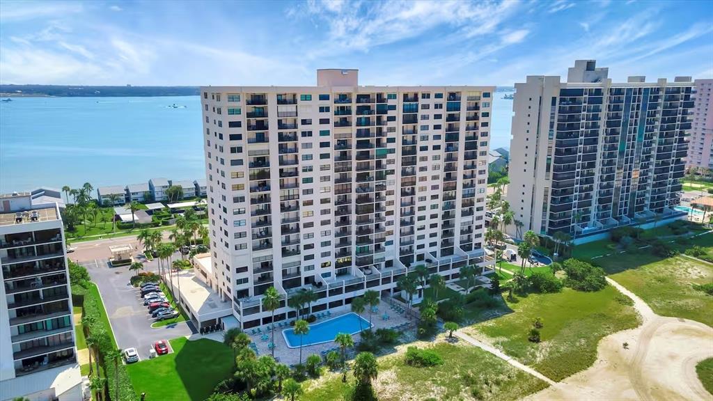 An aerial view shows two tall residential buildings with a swimming pool and coastal surroundings — 1270 GULF BOULEVARD UNIT 701, CLEARWATER BEACH, FL