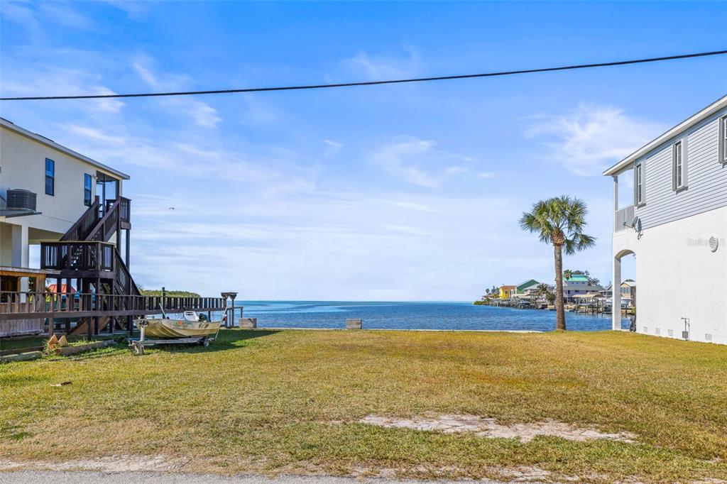 A vacant waterfront lot sits between two elevated houses with a small boat on a trailer — MCDONALD LN, HUDSON, FL