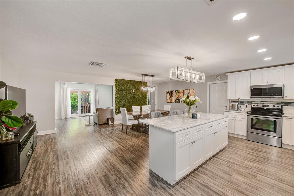An open-concept kitchen and dining area featuring a marble-topped island, white cabinetry, and wood flooring — 11288 60TH AVENUE, SEMINOLE, FL