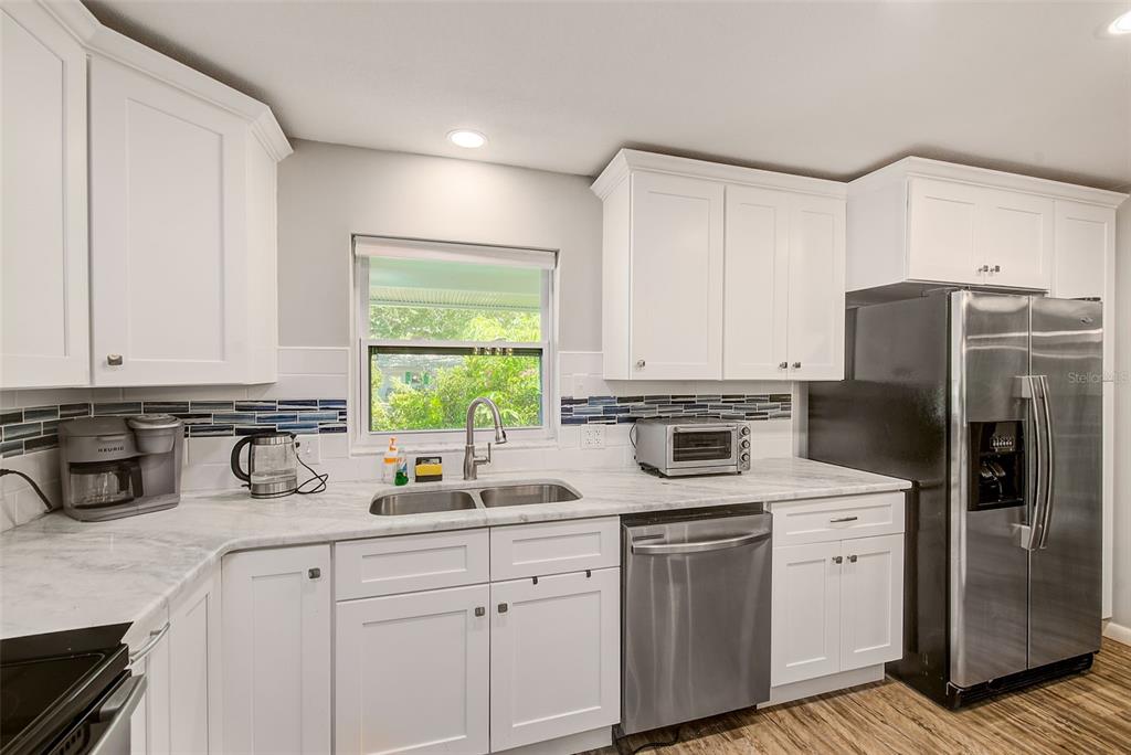 A kitchen with white cabinets, marble-look countertops, stainless steel appliances, and a blue tile backsplash — 11288 60TH AVENUE, SEMINOLE, FL