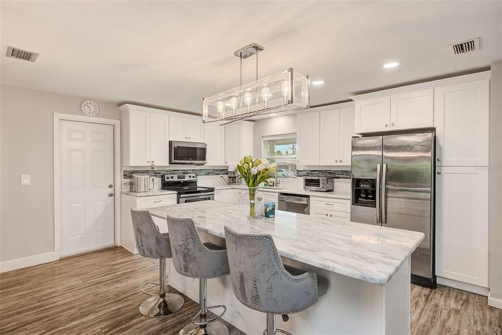 A kitchen features white cabinets, a marble-topped island with three gray stools, and stainless appliances — 11288 60TH AVENUE, SEMINOLE, FL