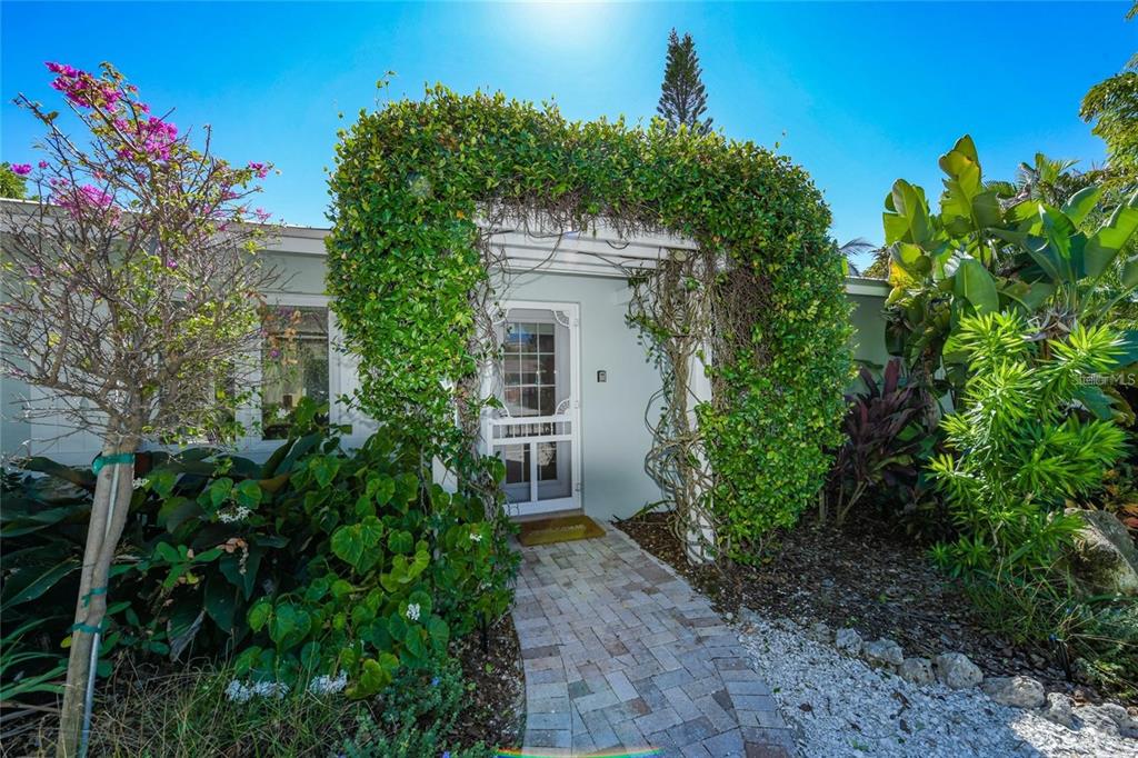 A brick walkway leads to a white front door framed by a lush green arbor — 207 PEACOCK LANE, HOLMES BEACH, FL