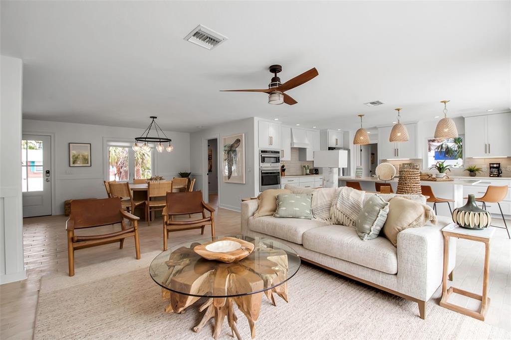 An open-concept living and dining area features light wood floors, a neutral sofa, and furniture — 207 PEACOCK LANE, HOLMES BEACH, FL