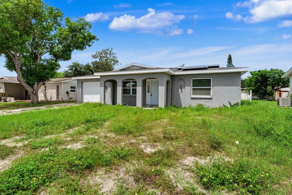 A single-story gray house with a white garage door and a large, overgrown front yard — 9517 MARLINTON LANE, PORT RICHEY, FL