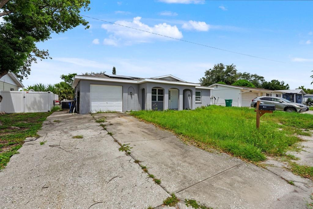 A single-story gray house with a concrete driveway and an overgrown lawn — 9517 MARLINTON LANE, PORT RICHEY, FL