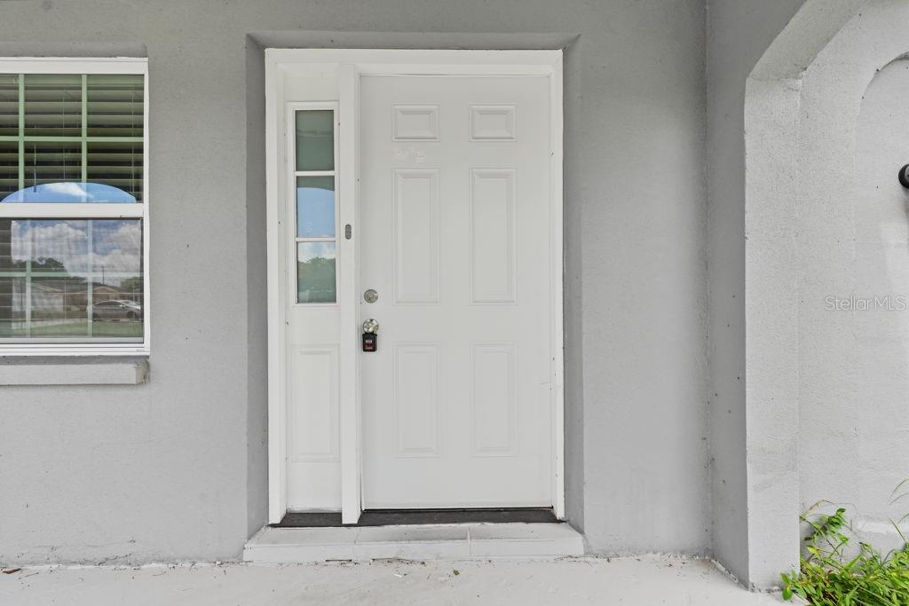 A white front door with a side window and a keypad lock on a porch — 9517 MARLINTON LANE, PORT RICHEY, FL