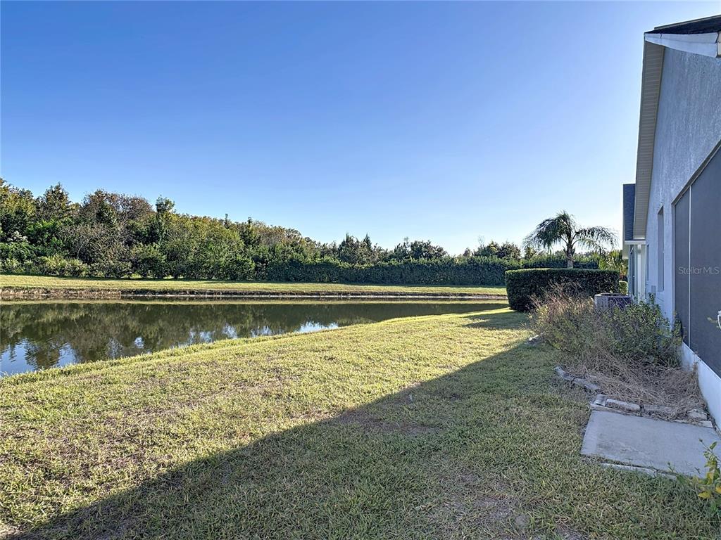 A view of a grassy backyard overlooking a pond with a house exterior on the right — 530 CORAL TRACE BOULEVARD, EDGEWATER, FL