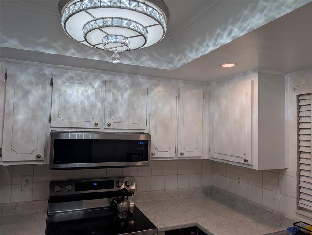A kitchen features white cabinets, a stainless steel microwave, and a decorative crystal ceiling light — 1100 E BAY DRIVE UNIT 96, LARGO, FL