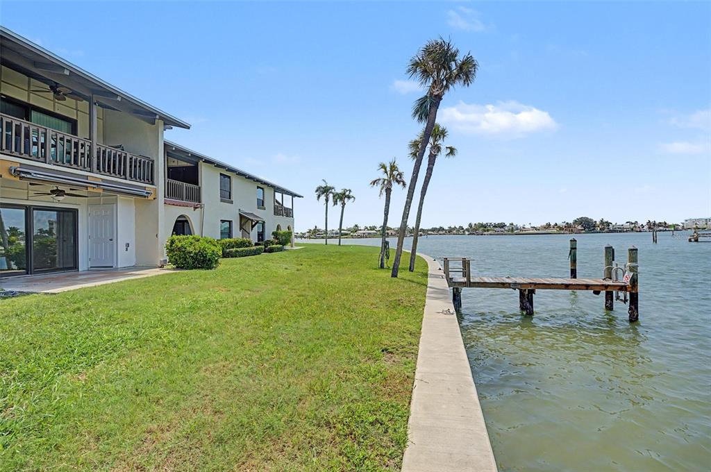 A multi-story building with balconies sits beside a grassy lawn, a concrete seawall, and a dock — 519 PLAZA SEVILLE COURT UNIT 39, TREASURE ISLAND, FL