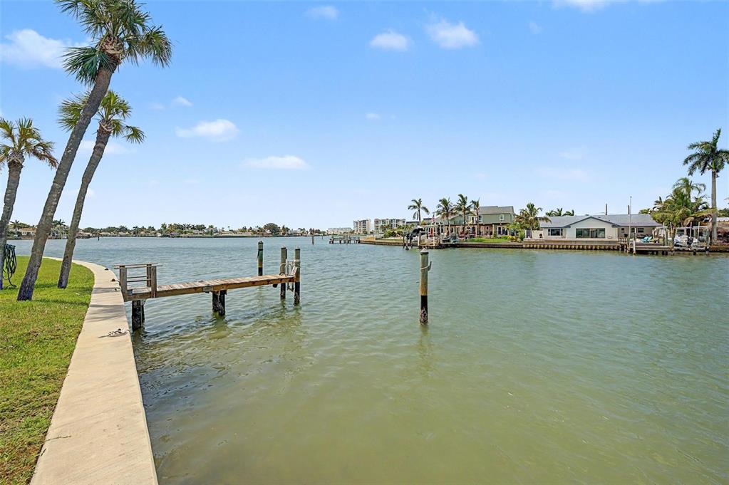 A wooden dock extends into a calm waterway with houses and palm trees in the background — 519 PLAZA SEVILLE COURT UNIT 39, TREASURE ISLAND, FL