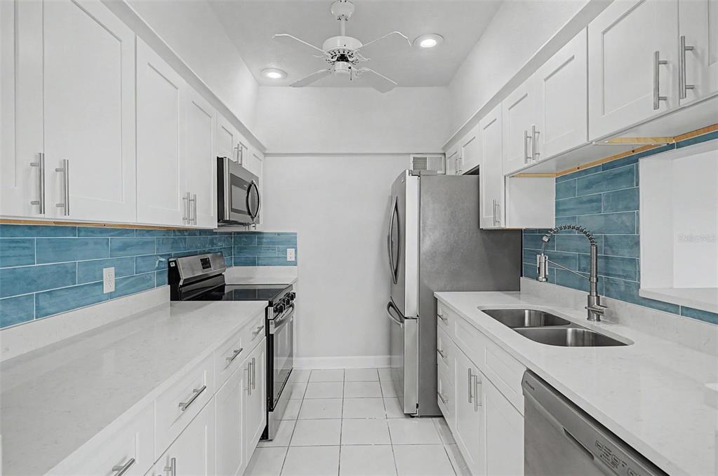 A galley kitchen features white cabinets, stainless steel appliances, white countertops, and blue tile backsplashes — 519 PLAZA SEVILLE COURT UNIT 39, TREASURE ISLAND, FL