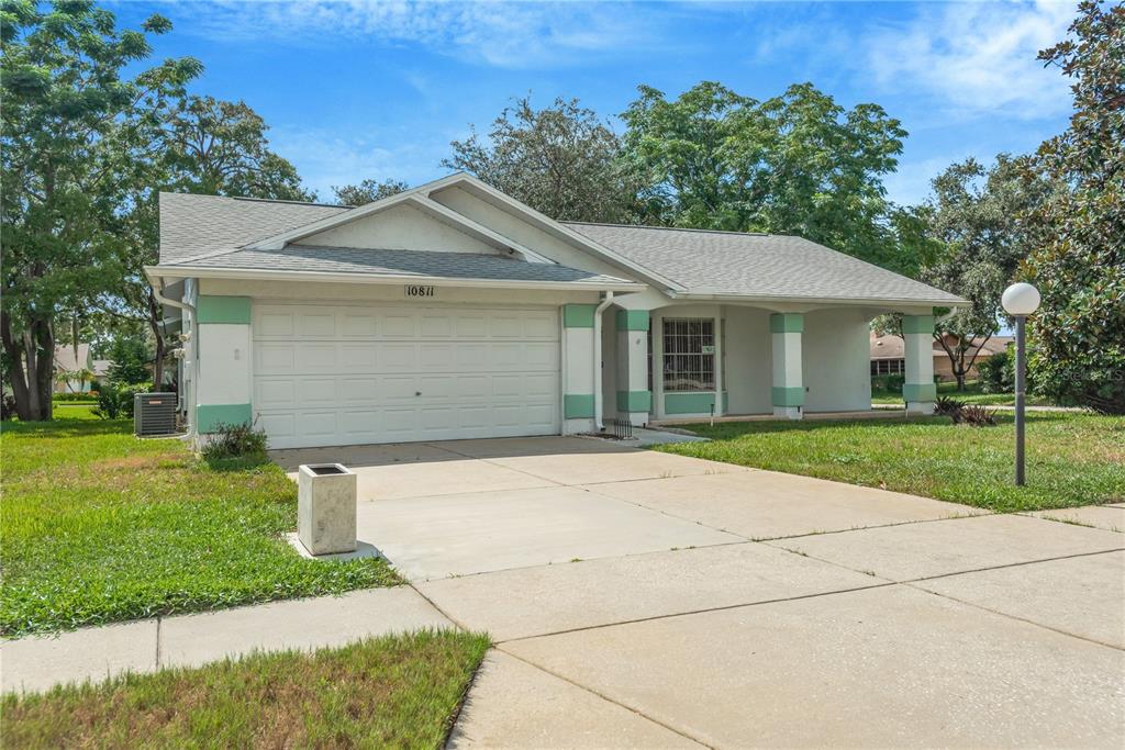 A single-story house with a white garage door, light-colored stucco walls, and green trim — 10811 PEPPERTREE LANE, PORT RICHEY, FL