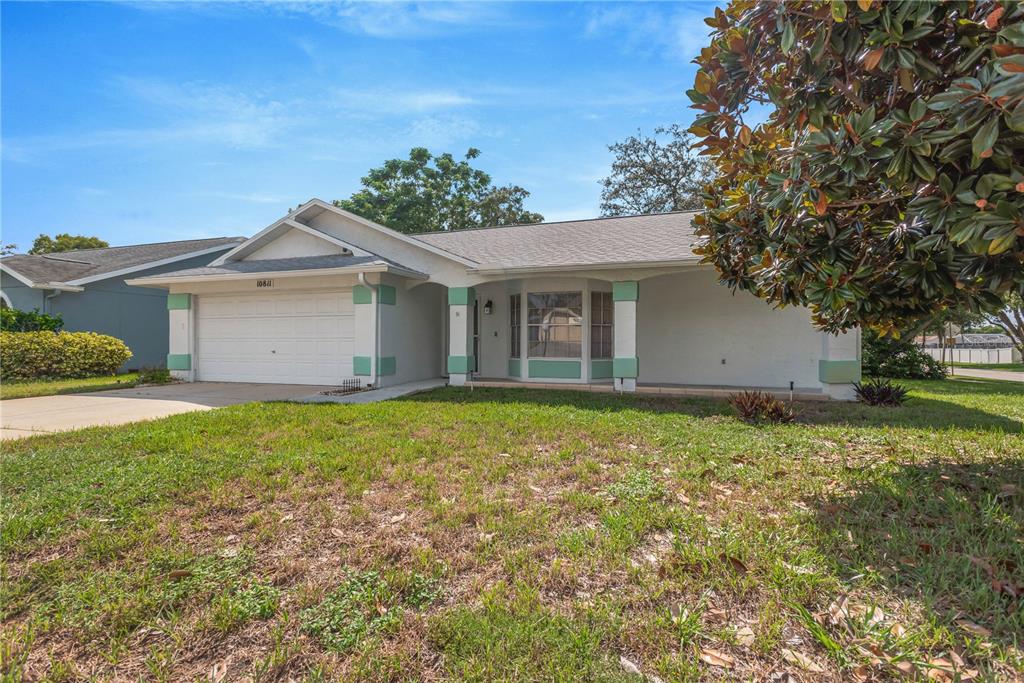 A single-story house with a white garage, light-colored stucco walls, and a green-trimmed front porch — 10811 PEPPERTREE LANE, PORT RICHEY, FL