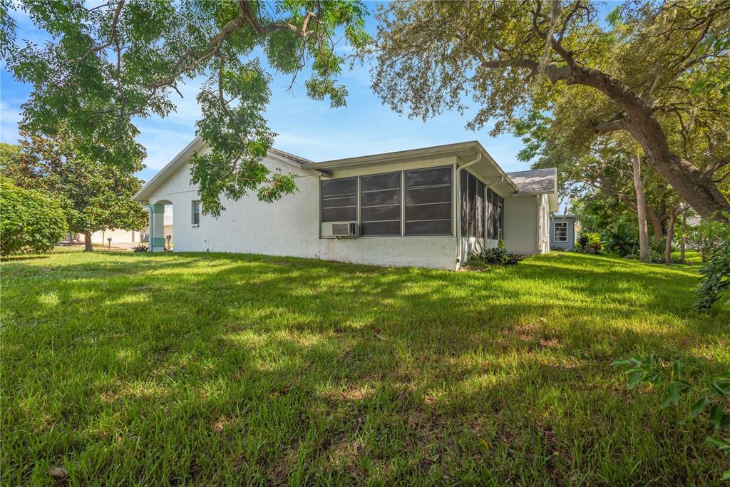 A white house with a screened-in porch sits on a grassy lot under large trees — 10811 PEPPERTREE LANE, PORT RICHEY, FL