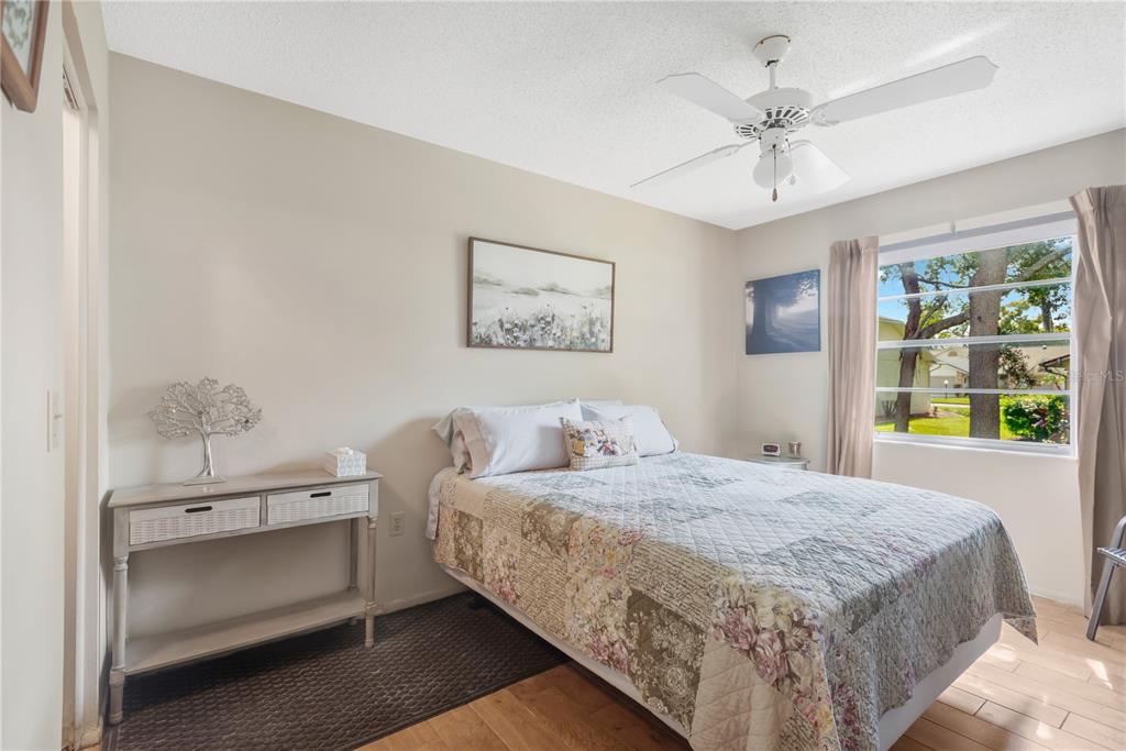 A bedroom features a bed with a floral quilt, a ceiling fan, and a console table — 10811 PEPPERTREE LANE, PORT RICHEY, FL