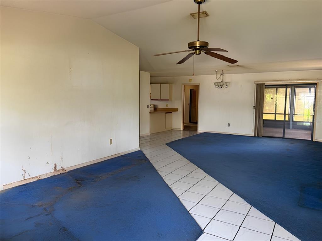 An open-concept living area features blue carpeting, white tile flooring, and a ceiling fan — 20 WOODBURY DRIVE, PALM COAST, FL