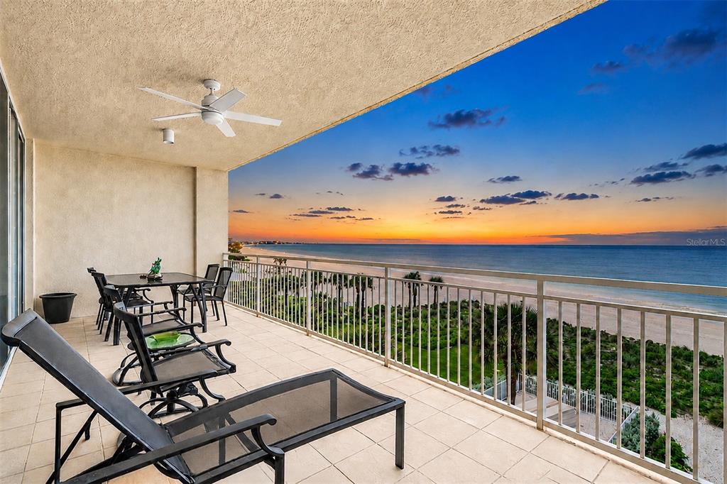 A balcony with outdoor furniture overlooks a sandy beach and ocean at sunset — 15208 GULF BOULEVARD UNIT 404, MADEIRA BEACH, FL