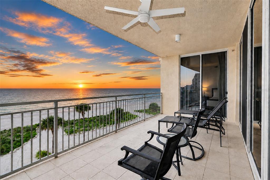 A balcony with patio furniture overlooks a beach and ocean at sunset under a ceiling fan — 15208 GULF BOULEVARD UNIT 404, MADEIRA BEACH, FL
