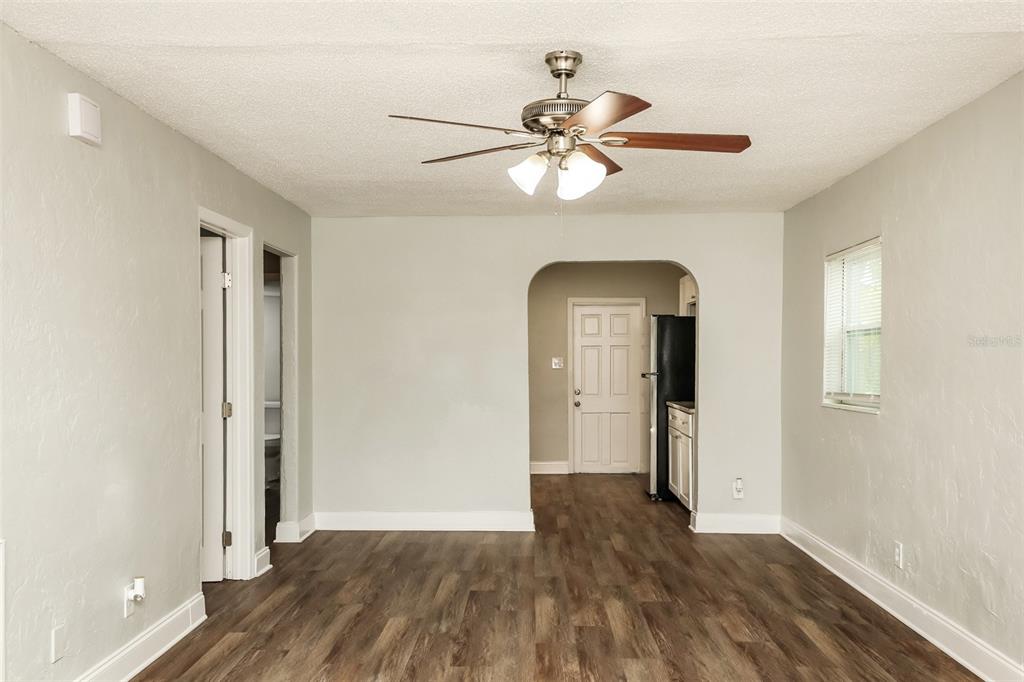 An empty room with wood-look flooring, a ceiling fan, and an arched doorway to the kitchen — 2624 13TH AVENUE S, ST PETERSBURG, FL