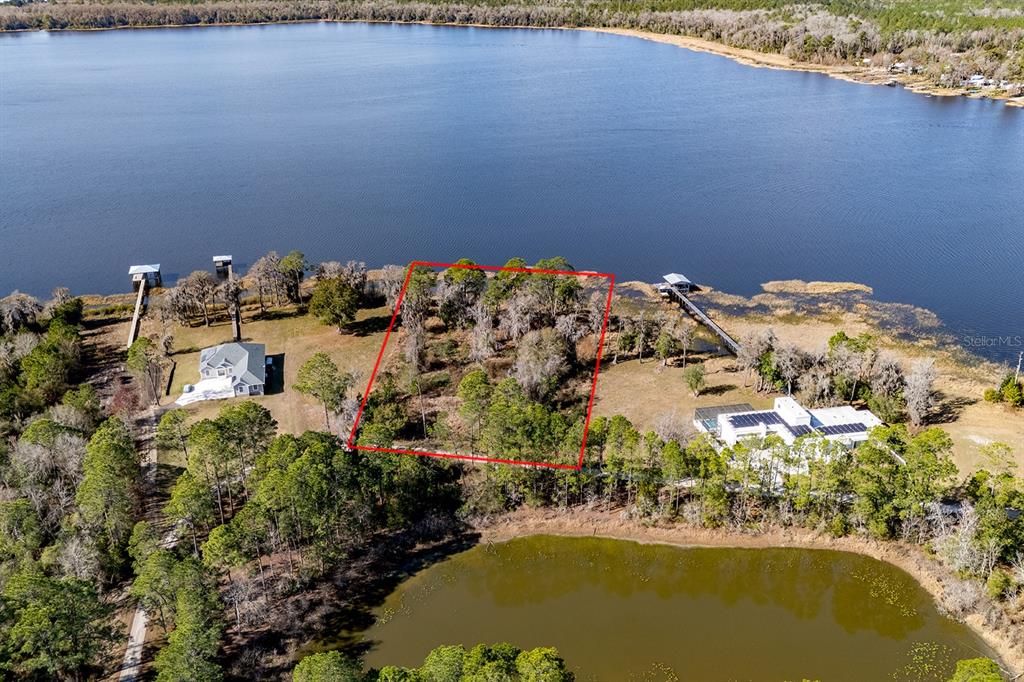 An aerial view shows a vacant, tree-covered lot outlined in red bordering a large lake — LAKESHORE DRIVE, STARKE, FL