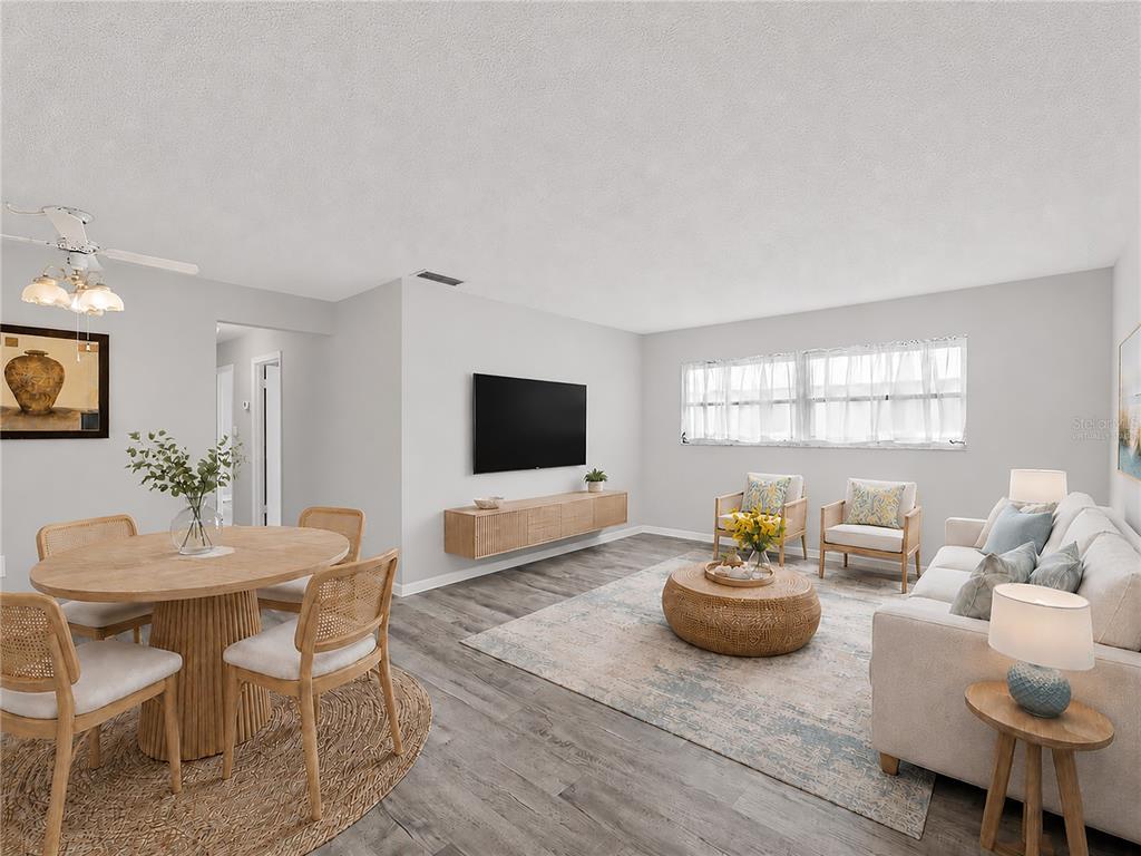 A living and dining area features light wood furniture, a wall-mounted television, and gray flooring — 460 BASE AVENUE E UNIT 128, VENICE, FL