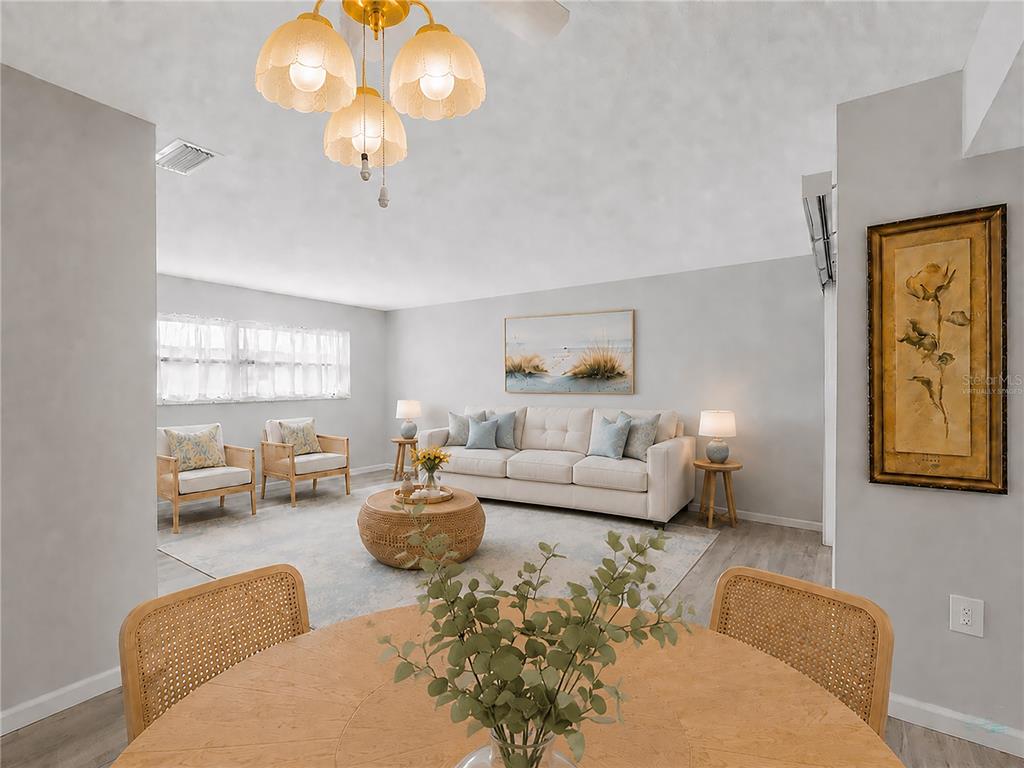 A living room with a sofa, two armchairs, and a dining table in the foreground — 460 BASE AVENUE E UNIT 128, VENICE, FL