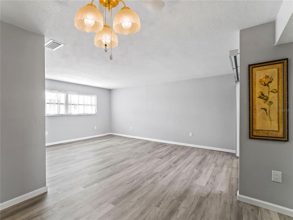An empty room features light gray walls, wood-look flooring, and a three-light brass chandelier — 460 BASE AVENUE E UNIT 128, VENICE, FL