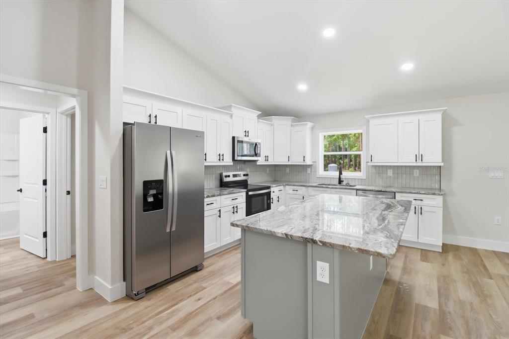 A modern kitchen features white cabinets, a gray island with a stone countertop, and stainless appliances — 1683 W PEARSON STREET, HERNANDO, FL
