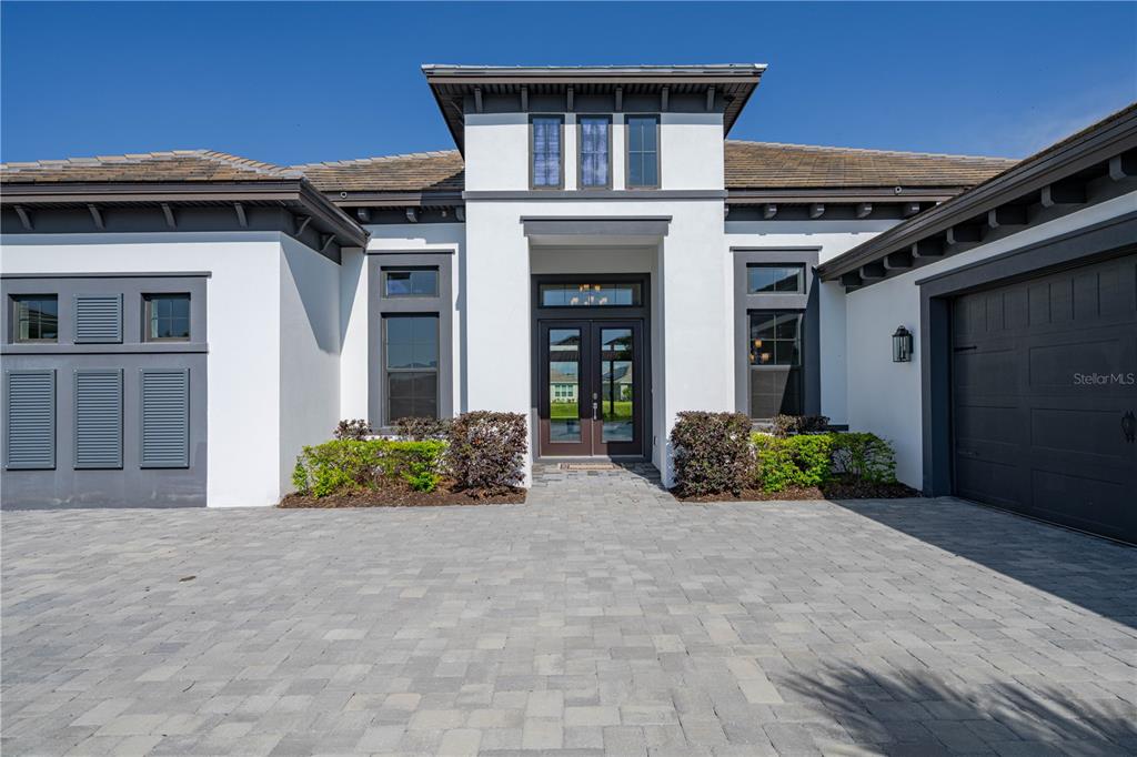 A modern single-story house features a white stucco exterior, dark trim, and a paved driveway — 4866 FRECCIA LOOP, WESLEY CHAPEL, FL