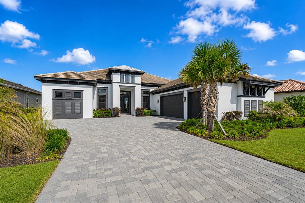 A modern single-story house with a paver driveway, dark garage doors, and a palm tree — 4866 FRECCIA LOOP, WESLEY CHAPEL, FL