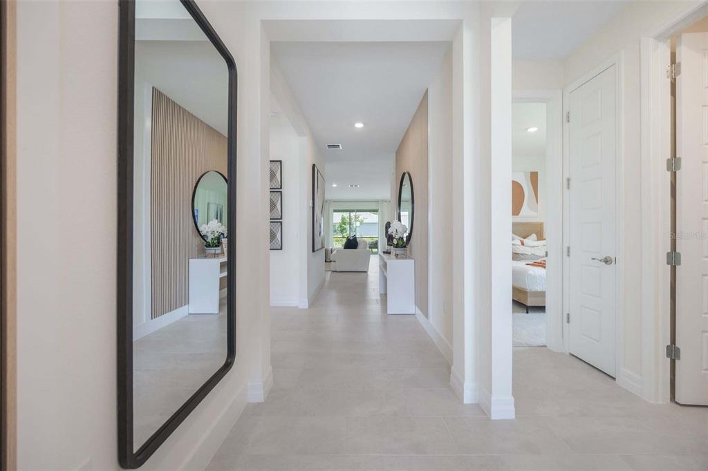 A bright hallway with light tile flooring leads toward a living area with a large mirror — 3949 KENNEBUNK LOOP, MOUNT DORA, FL