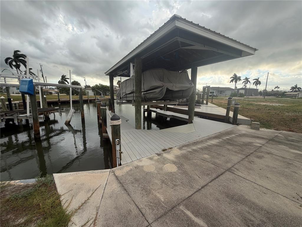 A boat lift with a covered boat sits above a wooden dock on a canal — 3881 ARECA DRIVE, ST JAMES CITY, FL