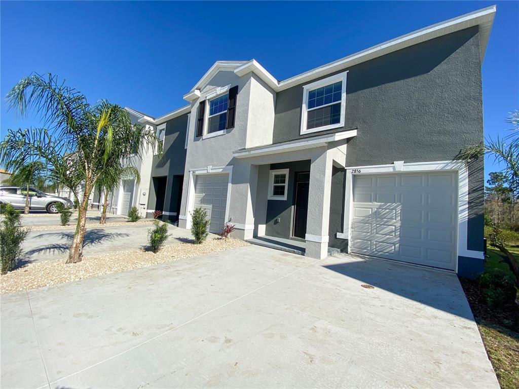 A two-story townhouse exterior with a gray stucco facade, white trim, and a concrete driveway — 2856 SUNCOAST BLEND DRIVE, ODESSA, FL