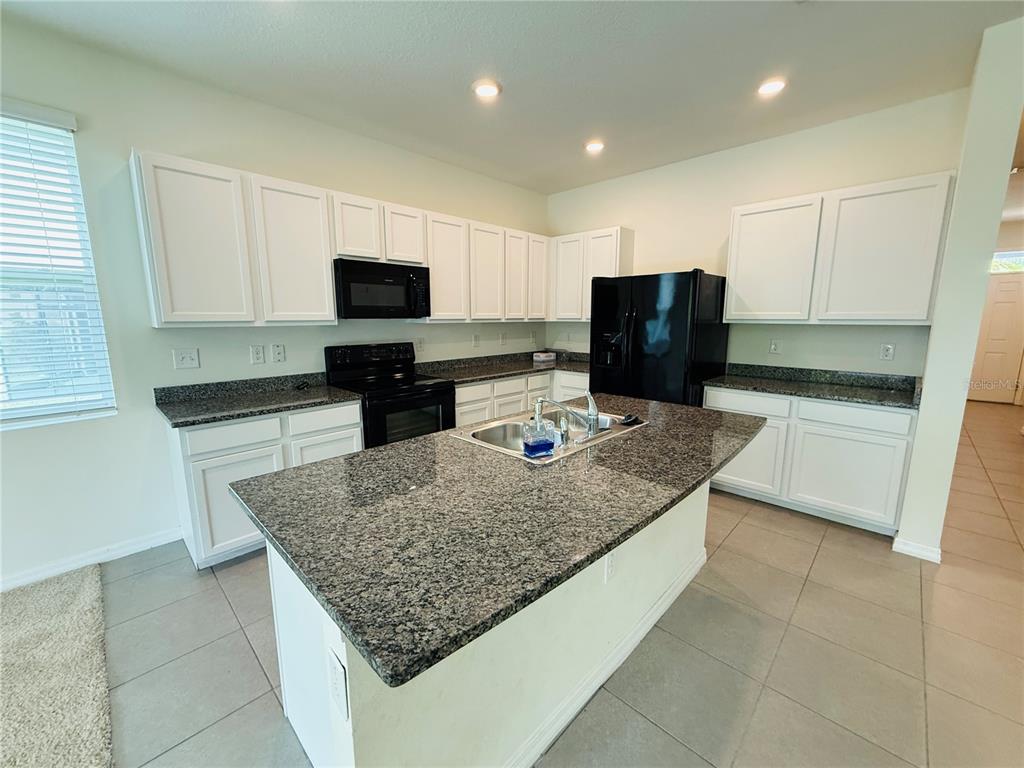 A kitchen features white cabinets, granite countertops, a center island, and black appliances — 2856 SUNCOAST BLEND DRIVE, ODESSA, FL
