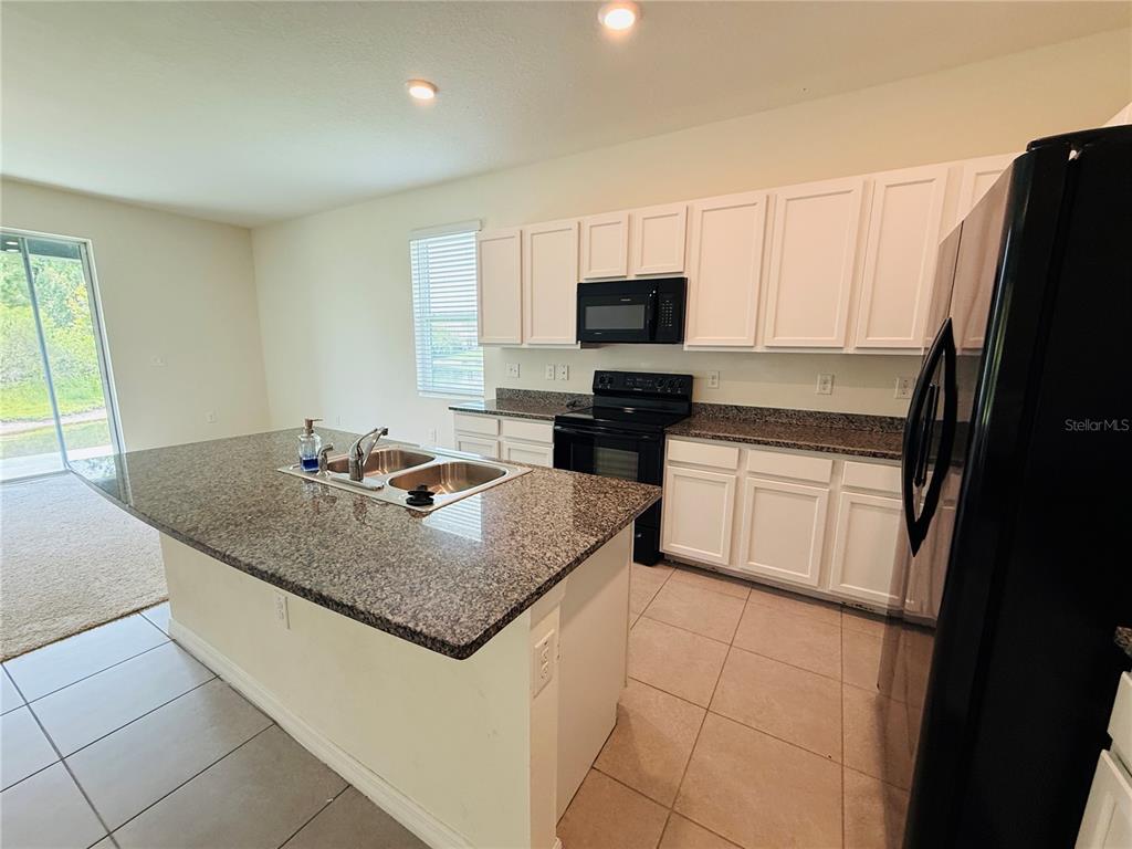 A kitchen features white cabinets, granite countertops, a center island, and black appliances — 2856 SUNCOAST BLEND DRIVE, ODESSA, FL