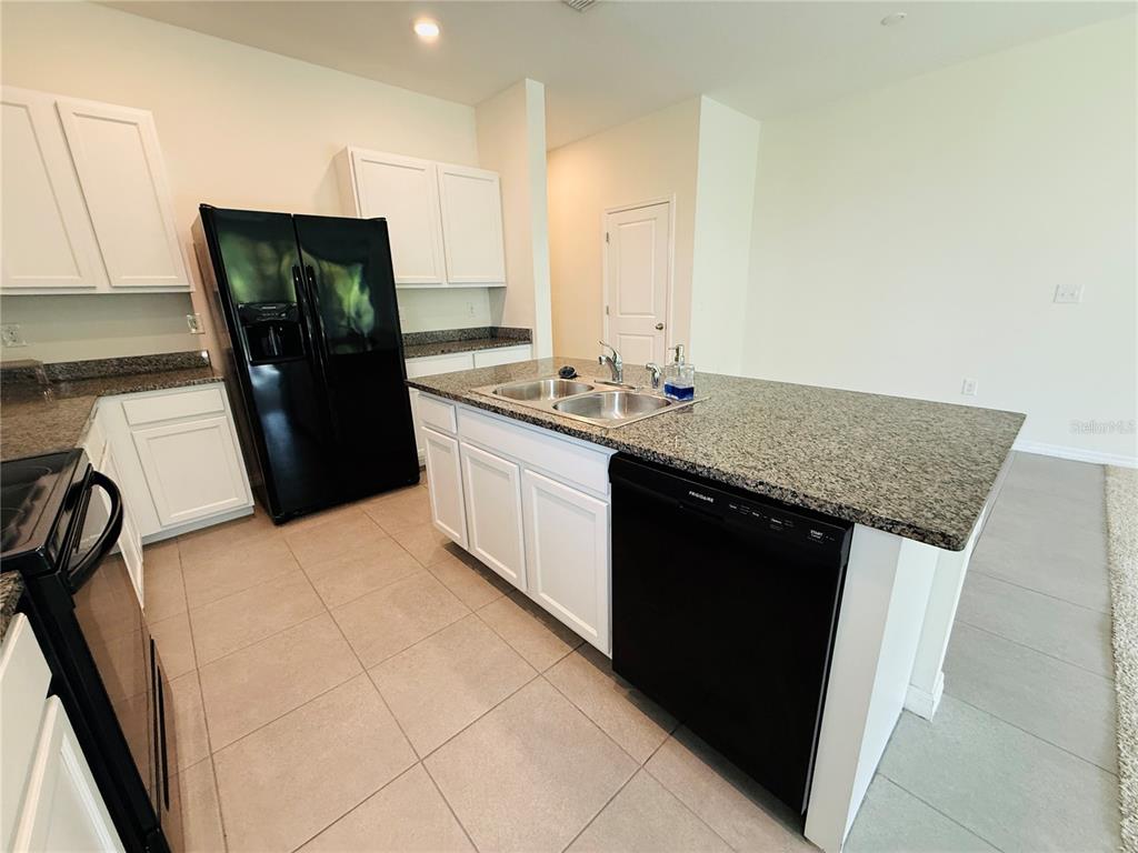 A kitchen features white cabinets, granite countertops, a black refrigerator, and a center island — 2856 SUNCOAST BLEND DRIVE, ODESSA, FL
