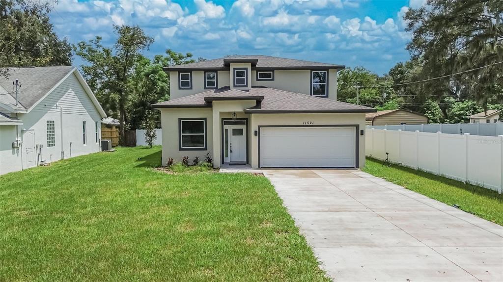 A two-story house with a beige exterior, a two-car garage, and a concrete driveway — 11521 HIGDON DRIVE, THONOTOSASSA, FL