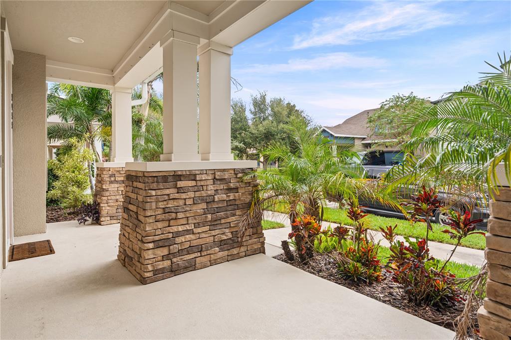 A covered front porch features stone-clad columns and a concrete floor overlooking a landscaped yard — 5955 CALDERA RIDGE DRIVE, LITHIA, FL