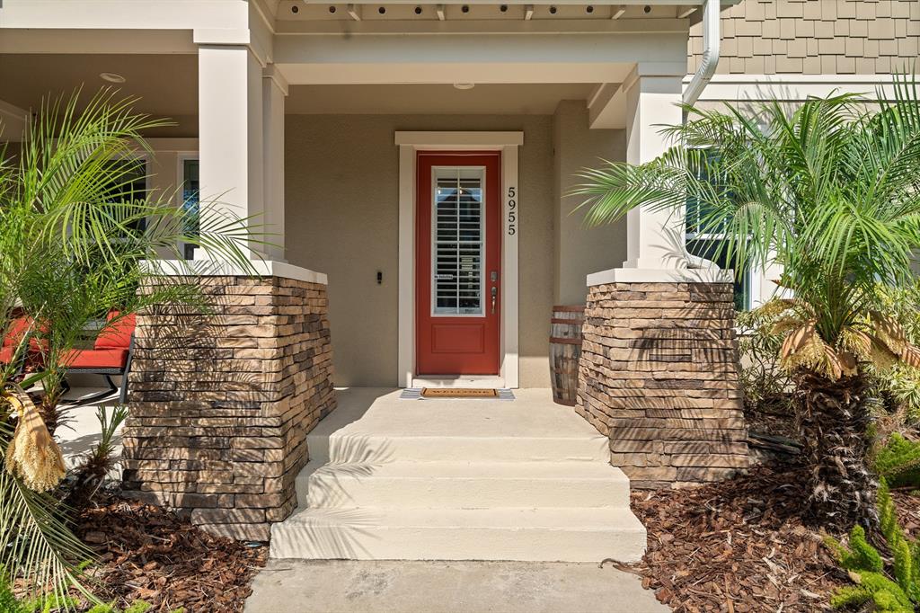 A front porch with stone pillars, a red door, and palm trees on either side — 5955 CALDERA RIDGE DRIVE, LITHIA, FL